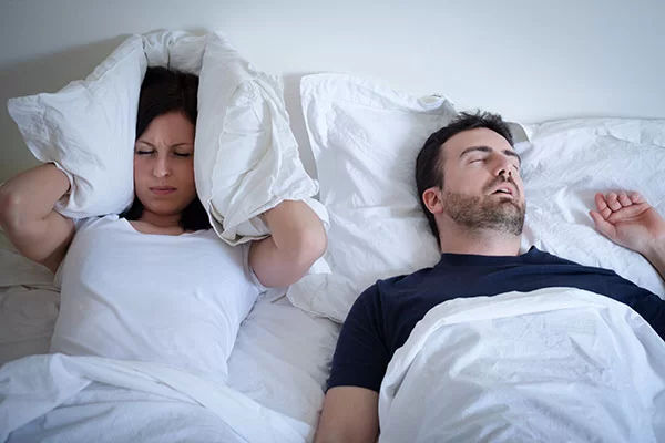 woman covering her ears with a pillow to block out her partner's loud snoring